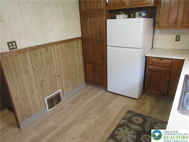 kitchen featuring visible vents, light countertops, freestanding refrigerator, wooden walls, and light wood-type flooring