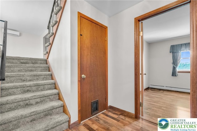staircase featuring baseboard heating, wood finished floors, and baseboards