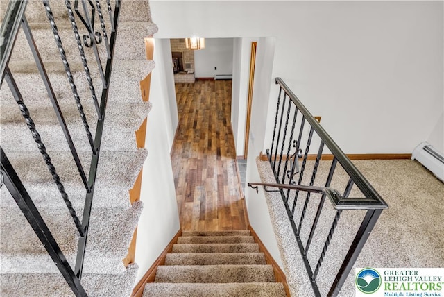 staircase with wood finished floors, baseboard heating, and baseboards