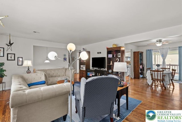 living room with visible vents, wood finished floors, and ceiling fan