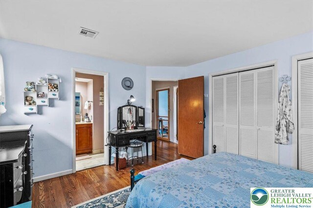 bedroom featuring wood finished floors, multiple closets, ensuite bathroom, baseboards, and visible vents