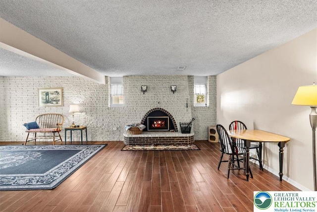 living area featuring a textured ceiling, wood finished floors, and brick wall