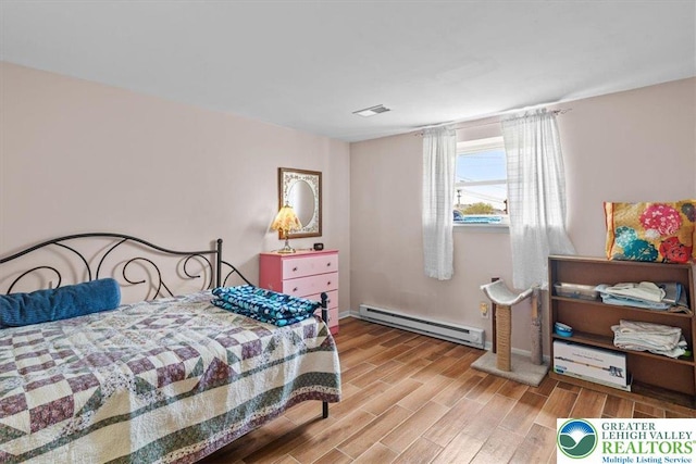 bedroom featuring wood finished floors, visible vents, and a baseboard heating unit
