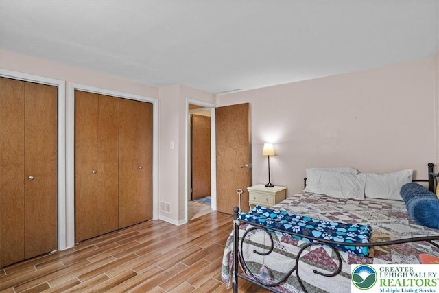 bedroom featuring baseboards, light wood-type flooring, visible vents, and two closets