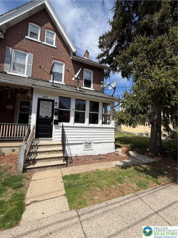 view of front of property featuring a chimney, a porch, and brick siding