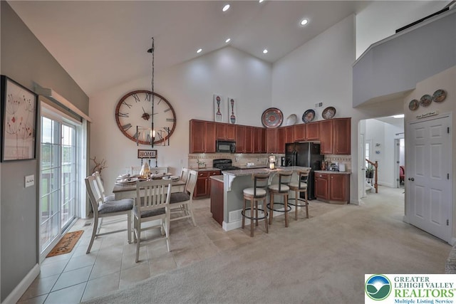 kitchen with decorative backsplash, a breakfast bar, a kitchen island, black appliances, and high vaulted ceiling
