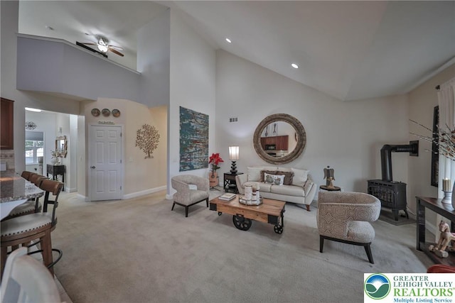 living room with a wood stove, ceiling fan, baseboards, light carpet, and high vaulted ceiling
