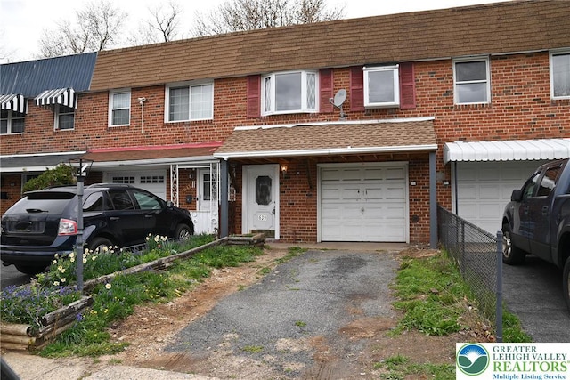 townhome / multi-family property with a garage, driveway, brick siding, roof with shingles, and fence