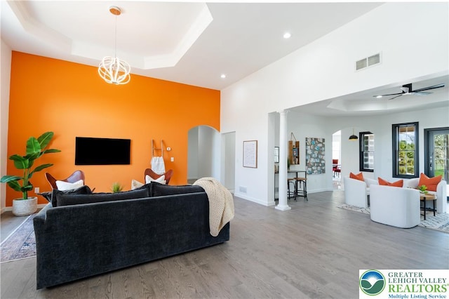 living room featuring recessed lighting, arched walkways, wood finished floors, visible vents, and a tray ceiling