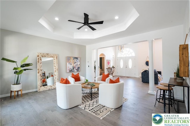 living area featuring a ceiling fan, arched walkways, wood finished floors, and a raised ceiling