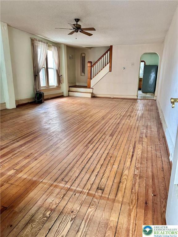 unfurnished living room with stairway, ceiling fan, light wood finished floors, and arched walkways