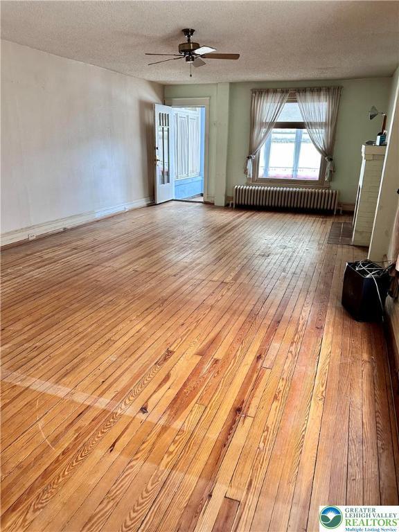 empty room featuring a textured ceiling, ceiling fan, hardwood / wood-style flooring, and radiator