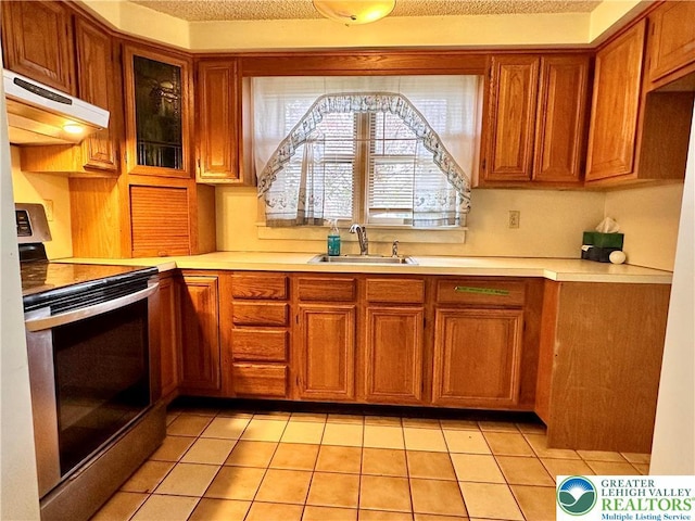 kitchen featuring electric stove, a sink, brown cabinetry, ventilation hood, and light countertops