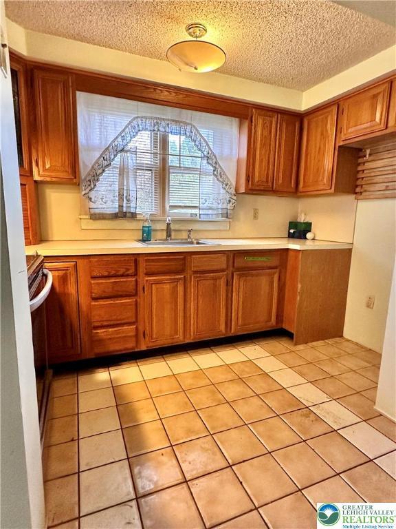 kitchen featuring light tile patterned floors, light countertops, brown cabinets, a sink, and a textured ceiling