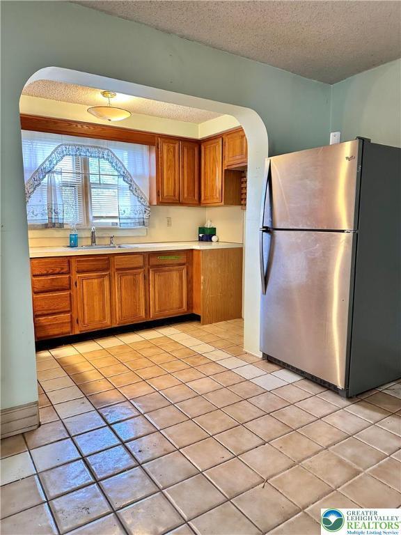 kitchen featuring a textured ceiling, light tile patterned floors, light countertops, freestanding refrigerator, and brown cabinetry