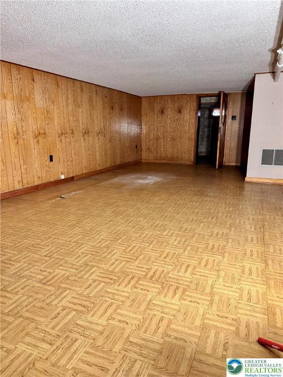 empty room with a textured ceiling, visible vents, wood walls, and baseboards
