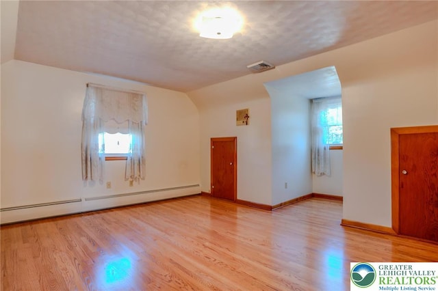 empty room featuring baseboard heating, light wood finished floors, baseboards, visible vents, and lofted ceiling