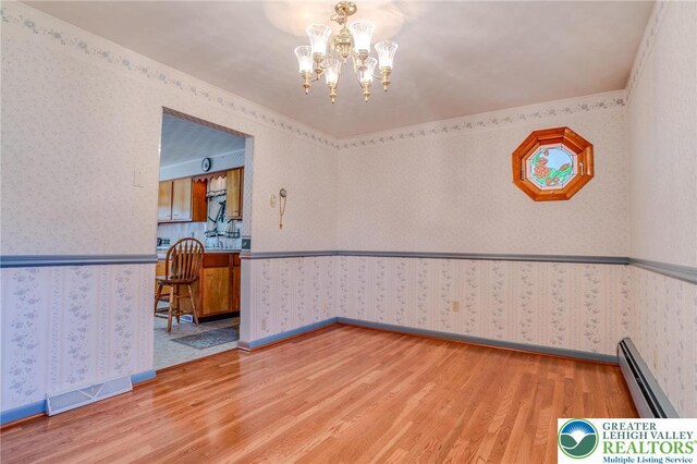 empty room featuring a baseboard radiator, light wood finished floors, and wallpapered walls