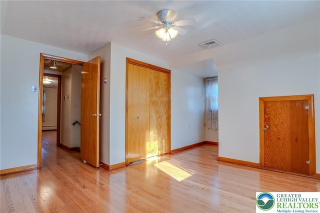 unfurnished bedroom featuring baseboard heating, visible vents, light wood-style floors, and baseboards