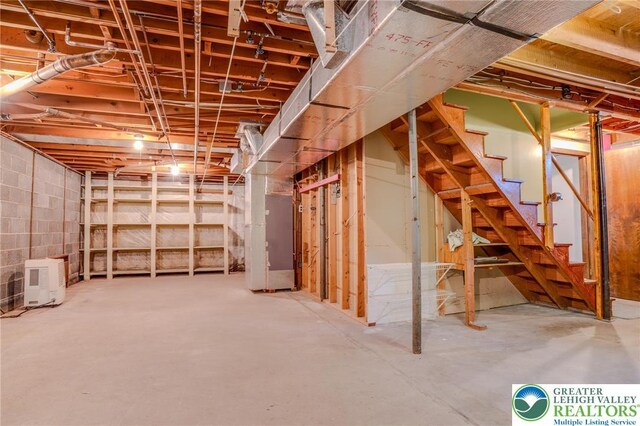 unfinished basement featuring stairway and heating unit