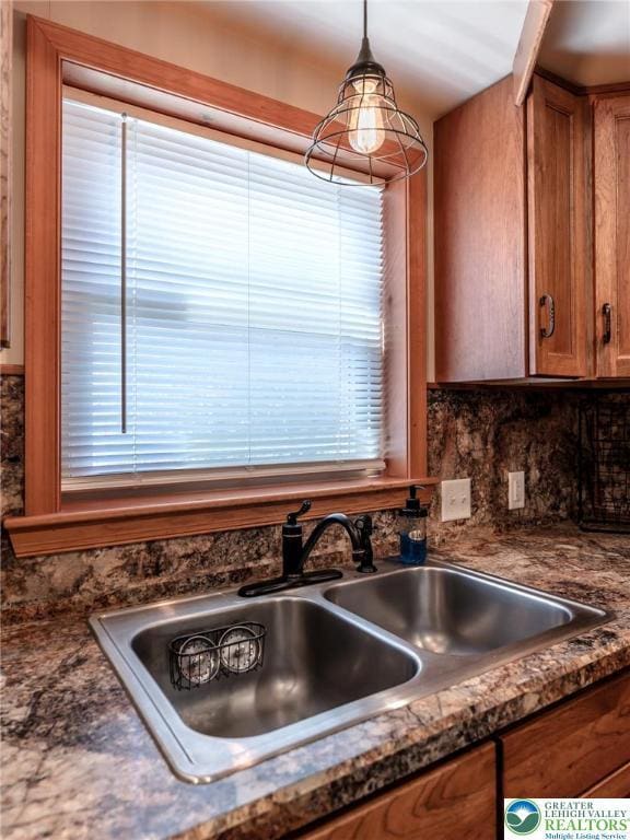 kitchen with dark countertops, a sink, brown cabinetry, decorative backsplash, and pendant lighting