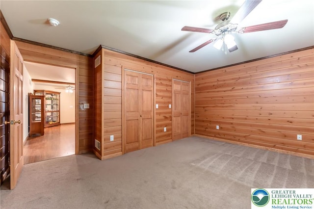 unfurnished bedroom featuring carpet floors, wood walls, a ceiling fan, and ornamental molding