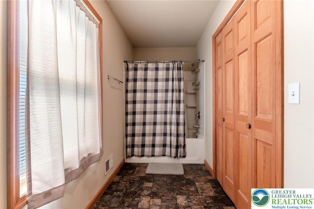full bath with baseboards, stone finish flooring, shower / bath combo, and visible vents