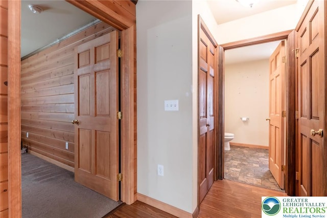 hall with baseboards, wood walls, and light wood finished floors