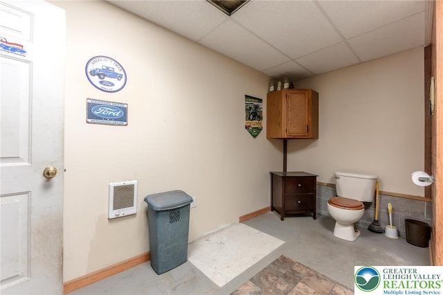 bathroom featuring heating unit, baseboards, a drop ceiling, and toilet