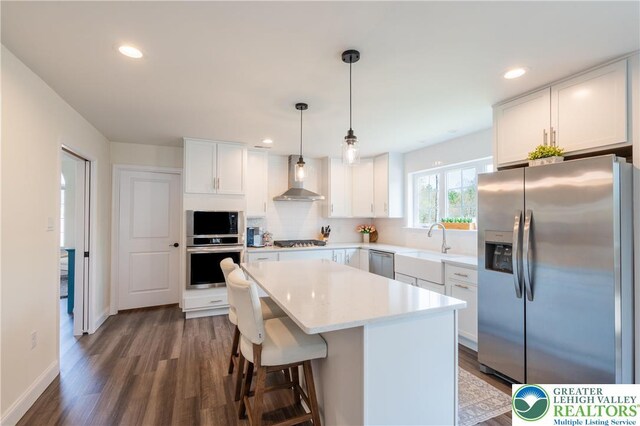131 Chinaberry Way, Polk Twp, PA 18058 - kitchen with wall chimney range hood, appliances with stainless steel finishes, a sink, dark wood finished floors, and a kitchen island