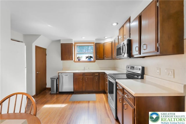 kitchen featuring a sink, light countertops, stainless steel appliances, recessed lighting, and light wood-type flooring