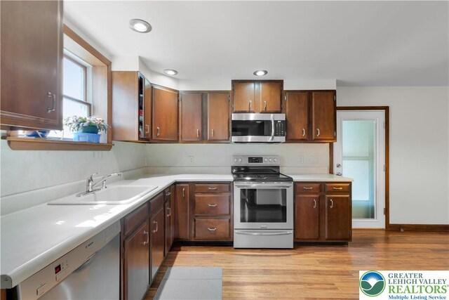 kitchen with a sink, light countertops, light wood finished floors, stainless steel appliances, and recessed lighting