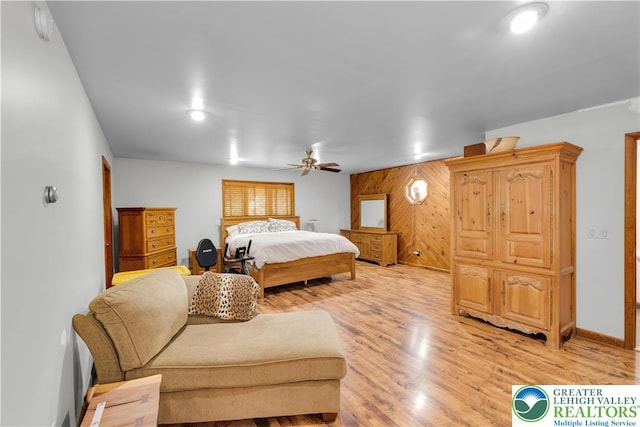 bedroom featuring ceiling fan, wood walls, baseboards, and light wood-type flooring