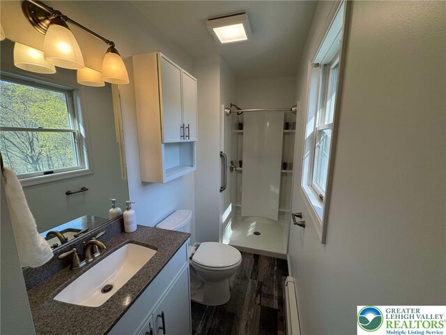 bathroom with vanity, toilet, wood finished floors, a baseboard heating unit, and a stall shower