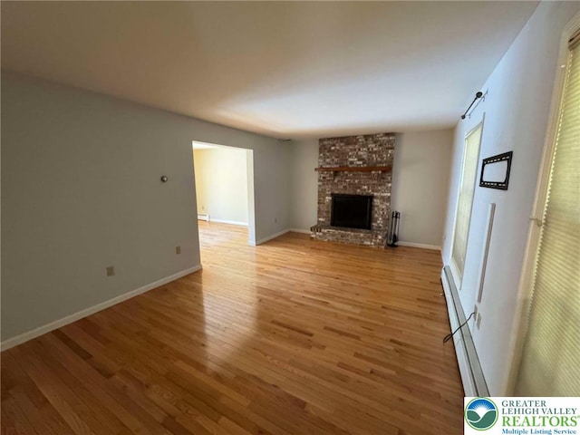 unfurnished living room featuring a fireplace, baseboard heating, baseboards, a baseboard heating unit, and light wood-style flooring