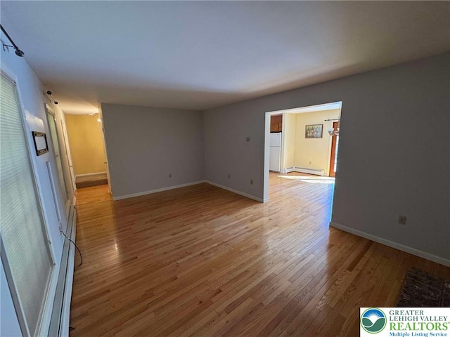 unfurnished room featuring baseboards, light wood-style flooring, and baseboard heating