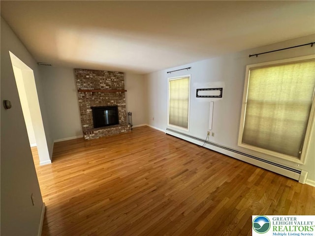 unfurnished living room featuring plenty of natural light, a baseboard radiator, a fireplace, and wood finished floors
