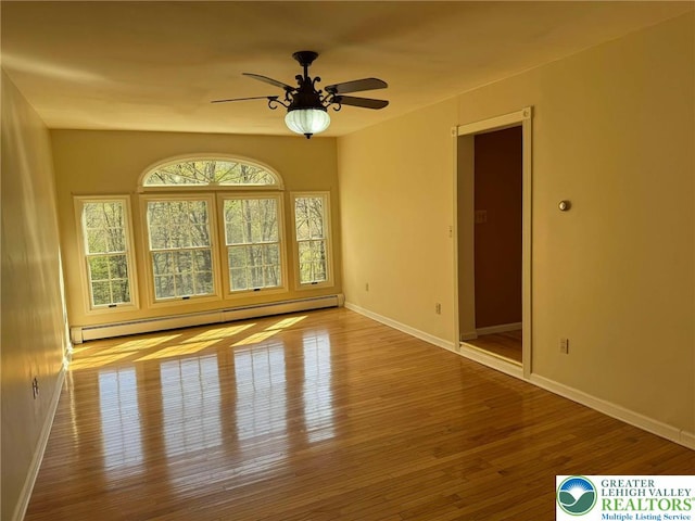 empty room featuring ceiling fan, a baseboard heating unit, baseboards, and hardwood / wood-style floors