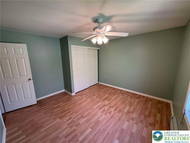 unfurnished bedroom featuring a ceiling fan, baseboards, wood finished floors, a baseboard radiator, and a closet