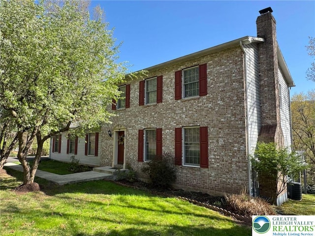 colonial-style house featuring cooling unit, a chimney, a front yard, and brick siding