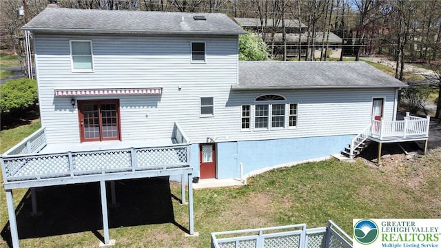 rear view of house with roof with shingles, a chimney, a lawn, and a deck