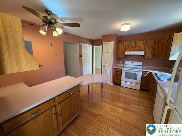 kitchen featuring ceiling fan, brown cabinets, a sink, under cabinet range hood, and white appliances
