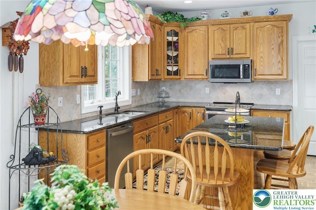 kitchen with a kitchen bar, a sink, glass insert cabinets, dark stone counters, and stainless steel appliances