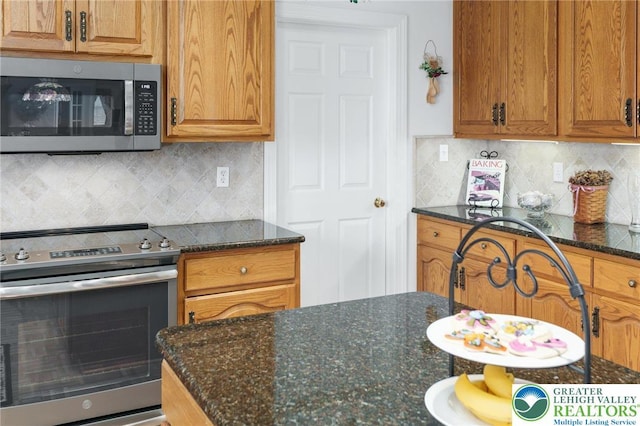 kitchen featuring brown cabinetry, dark stone counters, appliances with stainless steel finishes, and tasteful backsplash