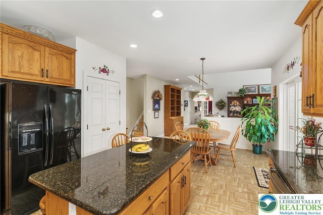 kitchen with hanging light fixtures, a center island, dark stone counters, recessed lighting, and black fridge with ice dispenser