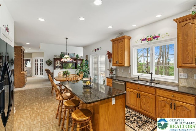 kitchen featuring a center island, black fridge with ice dispenser, a sink, a breakfast bar, and recessed lighting