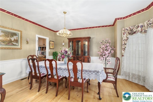 dining room featuring an inviting chandelier, crown molding, wood finished floors, and visible vents