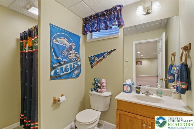 bathroom featuring vanity, baseboards, a drop ceiling, and toilet