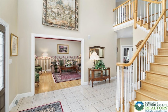 tiled foyer entrance featuring baseboards, stairs, a high ceiling, and visible vents