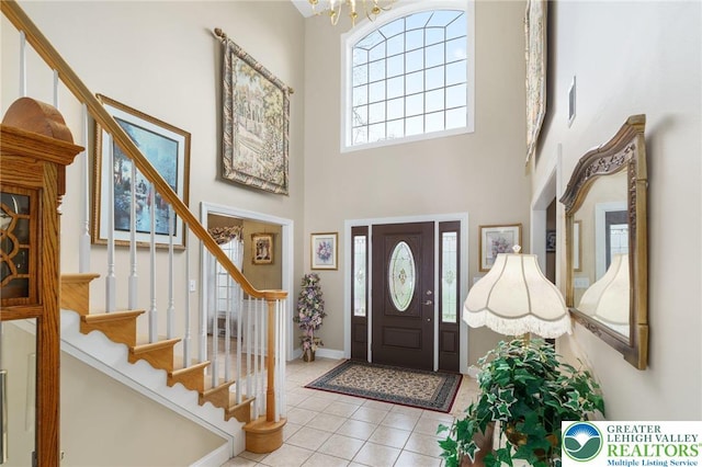 tiled foyer featuring an inviting chandelier, baseboards, a towering ceiling, and stairway